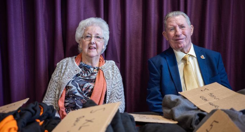 Woman with white hair sat smiling next to a man with dark hair smiling